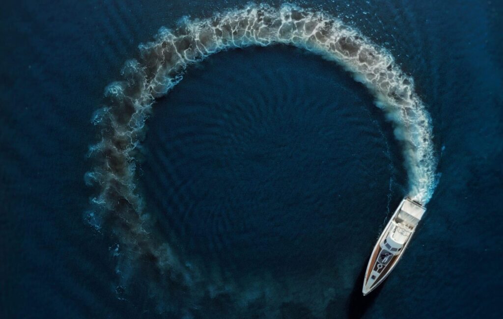 An aerial shot of a motorboat making a circular ripple pattern in the azure ocean water, showcasing motion and summer vibes.