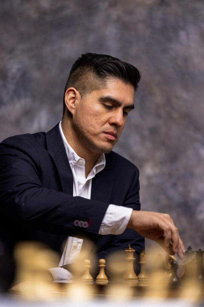 A focused man in a suit playing chess against a gray backdrop.
